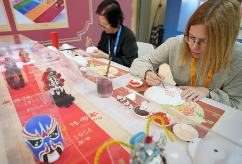 10月16日，在第三屆“一帶一路”國際合作高峰論壇新聞中心，來自比利時(shí)的記者（右）體驗(yàn)畫京劇臉譜。新華社記者 王毓國 攝