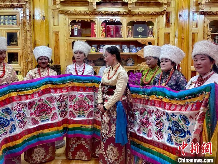 圖為女性展示村民自發(fā)繡制的“百米五彩哈達(dá)”?！±钣穹?攝