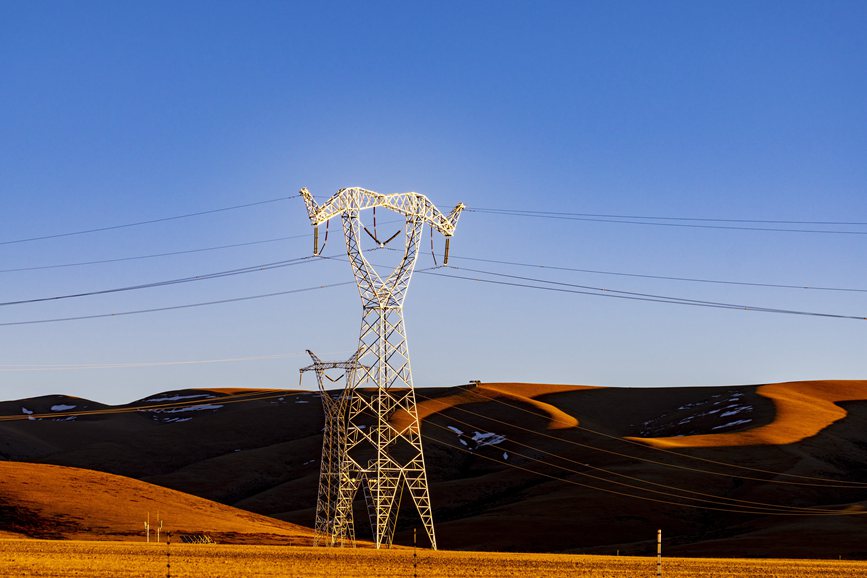 阿里地區(qū)的曠野上，電力鐵塔在夕陽下熠熠生輝。